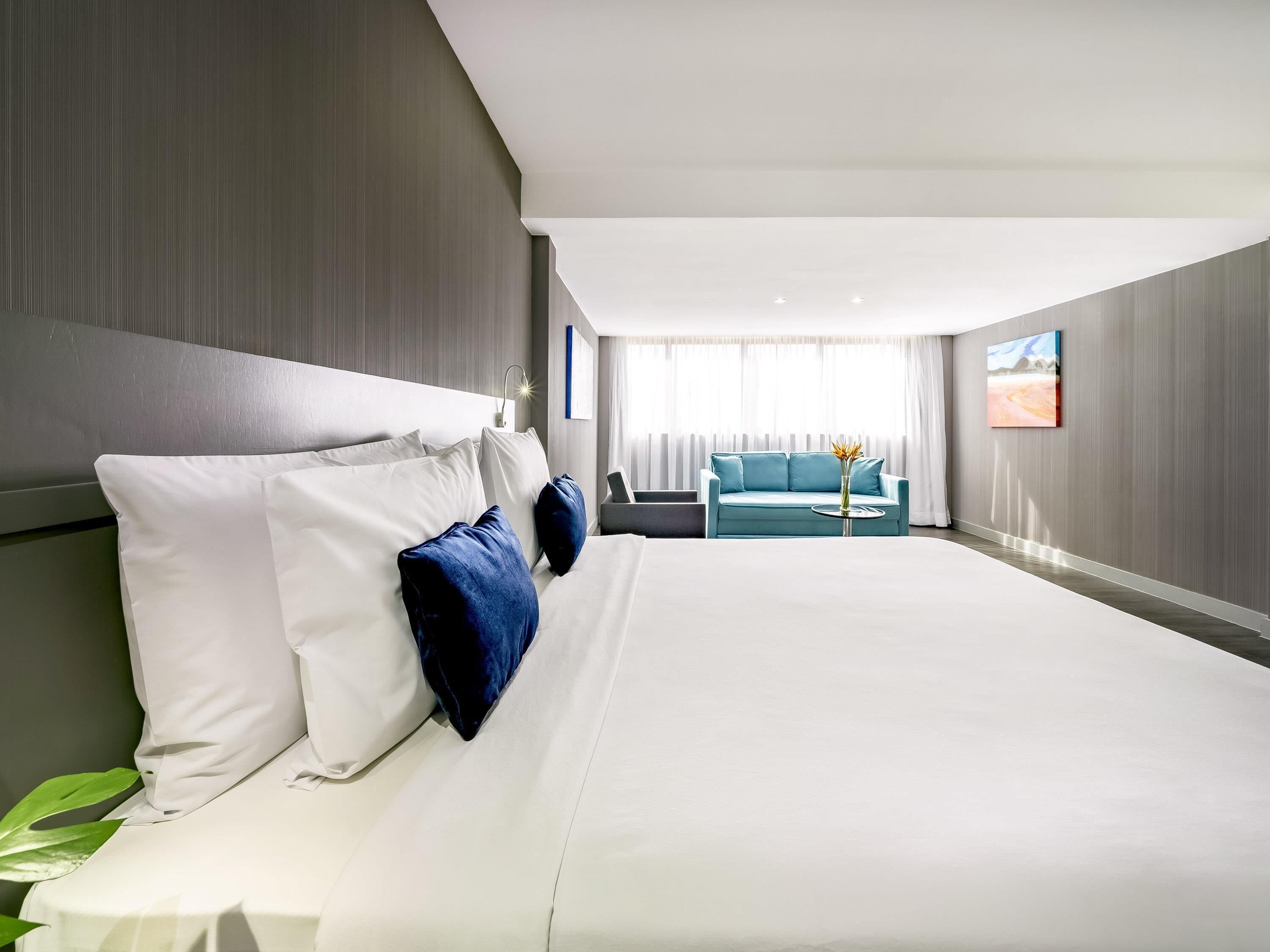 A modern hotel room with a large bed, a sofa, and a view of the outdoors.