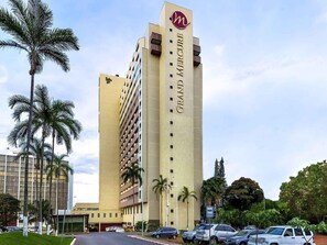 A tall hotel building with a prominent logo, multiple floors, and a parking area with cars. - Grand Mercure Brasilia Eixo Monumental (Brasília)