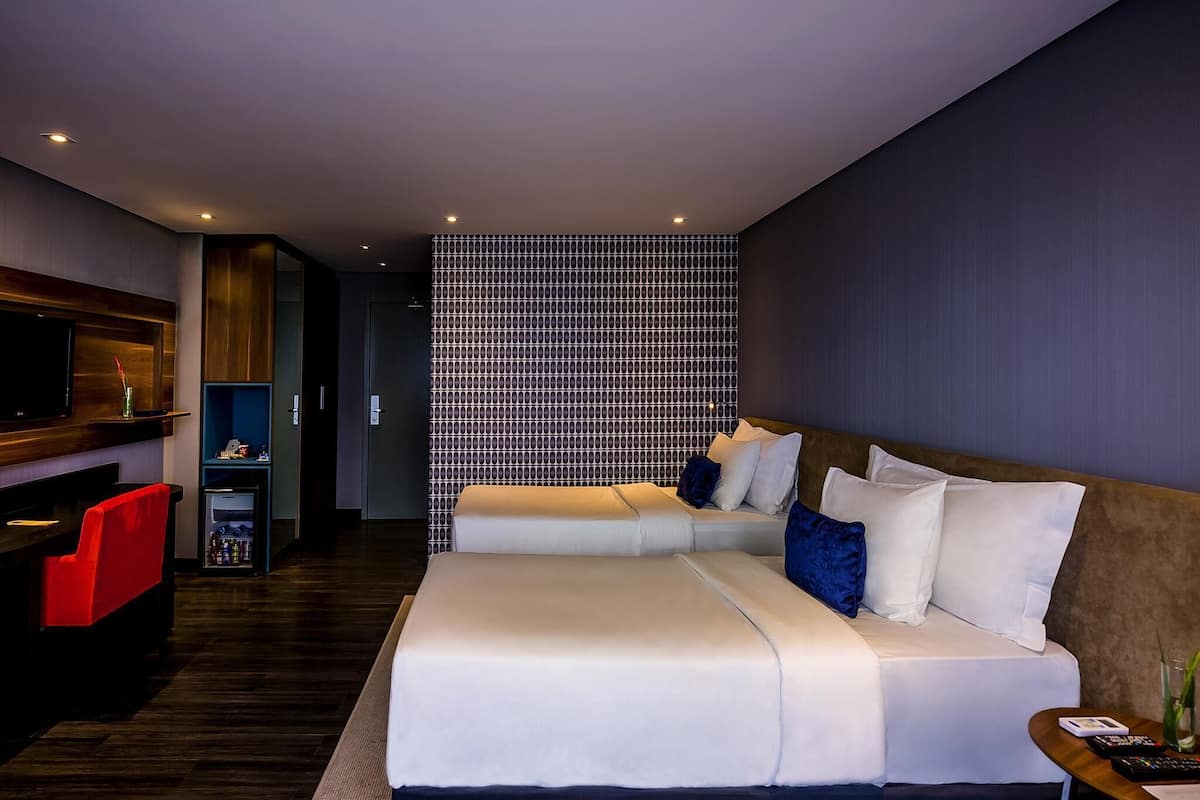 Quarto de hotel moderno com uma cama grande, TV, minibar e parede com padrão.