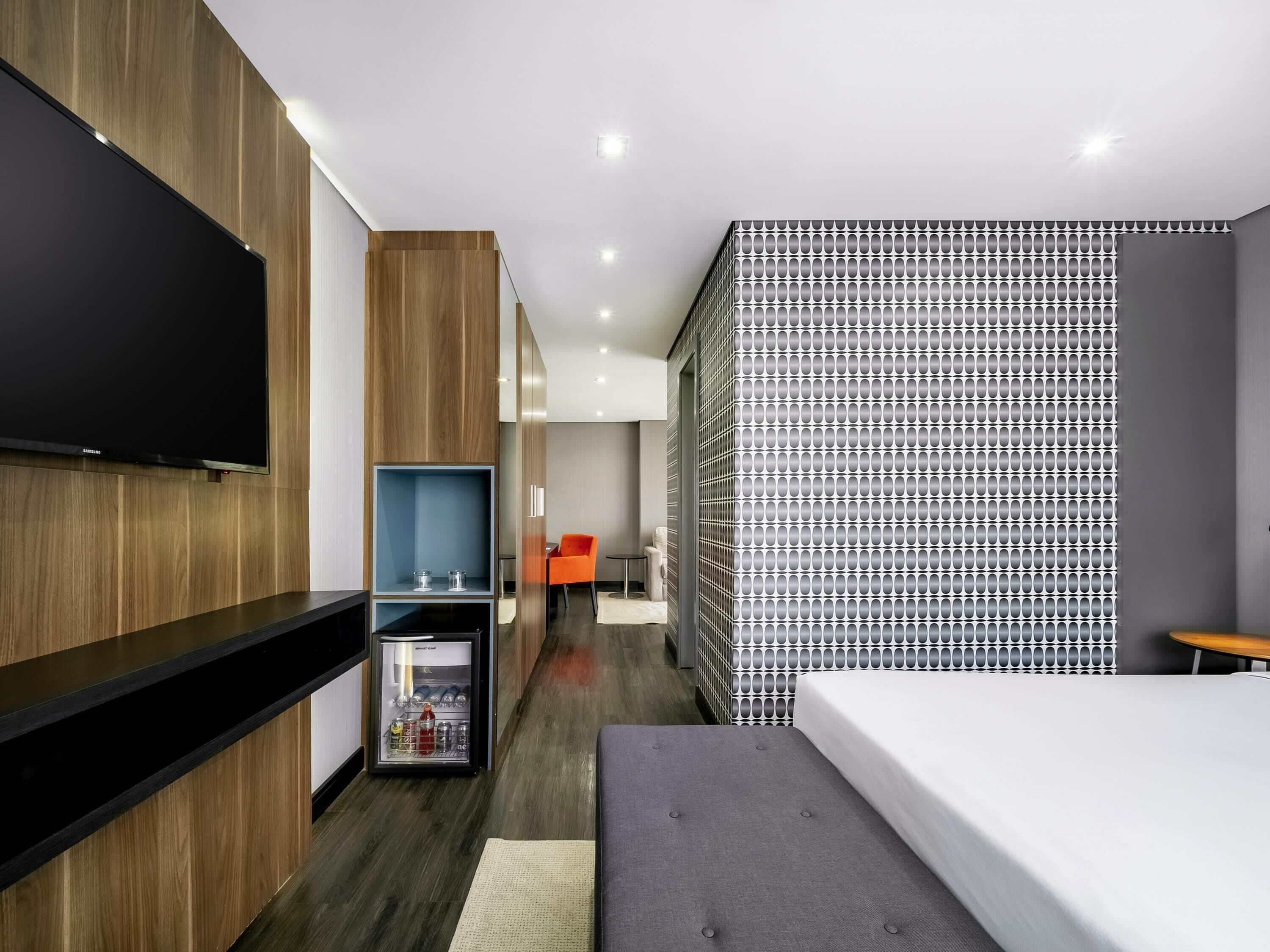 Une chambre d'hôtel moderne dotée d'une télévision à écran plat, d'un minibar, d'un canapé et d'un mur décoré de motifs.