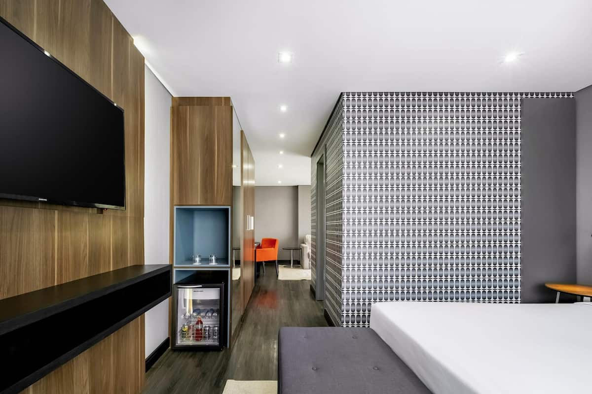 Une chambre d'hôtel moderne dotée d'une télévision à écran plat, d'un minibar, d'un canapé et d'un mur décoré de motifs.