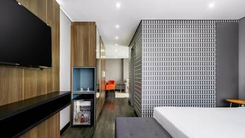 Ein modernes Hotelzimmer mit Flachbildfernseher, einer Minibar, einer Couch und einer Wand mit Muster.
