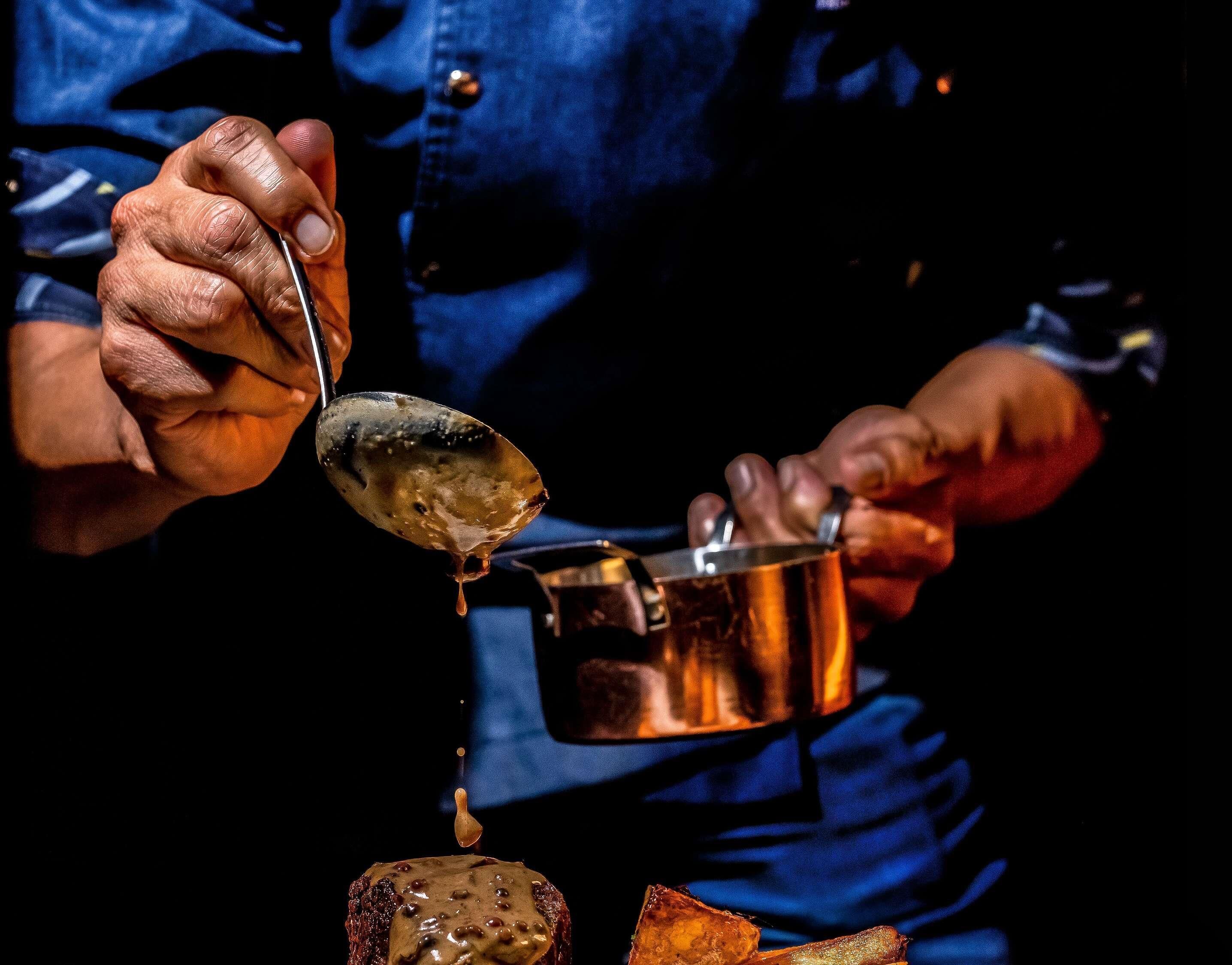 A person pouring sauce from a pot onto food.