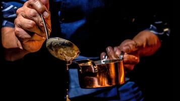 A person pouring sauce from a pot onto food.