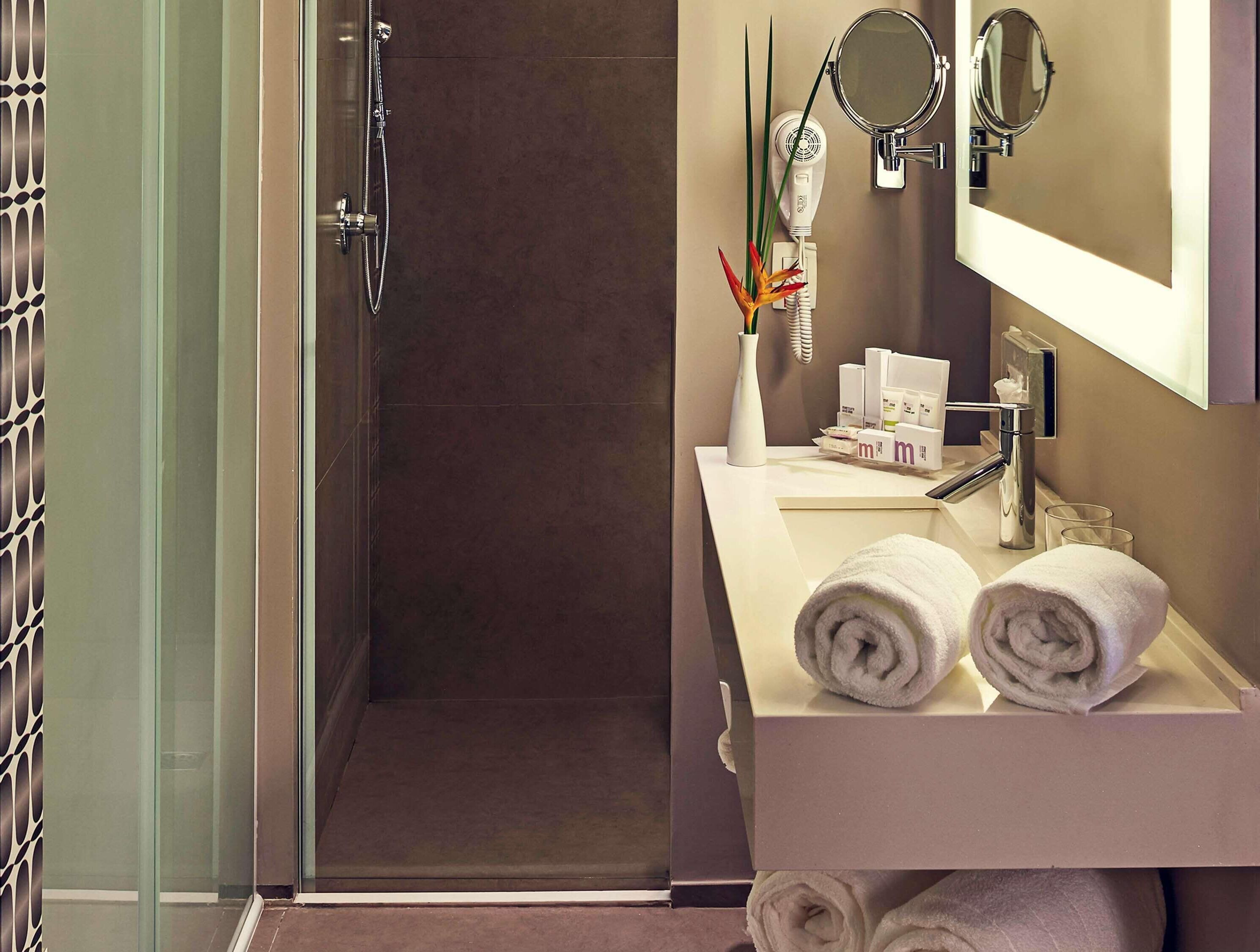 Un baño moderno con cabina de ducha de vidrio, un lavabo blanco con dos toallas, un espejo y artículos de aseo.