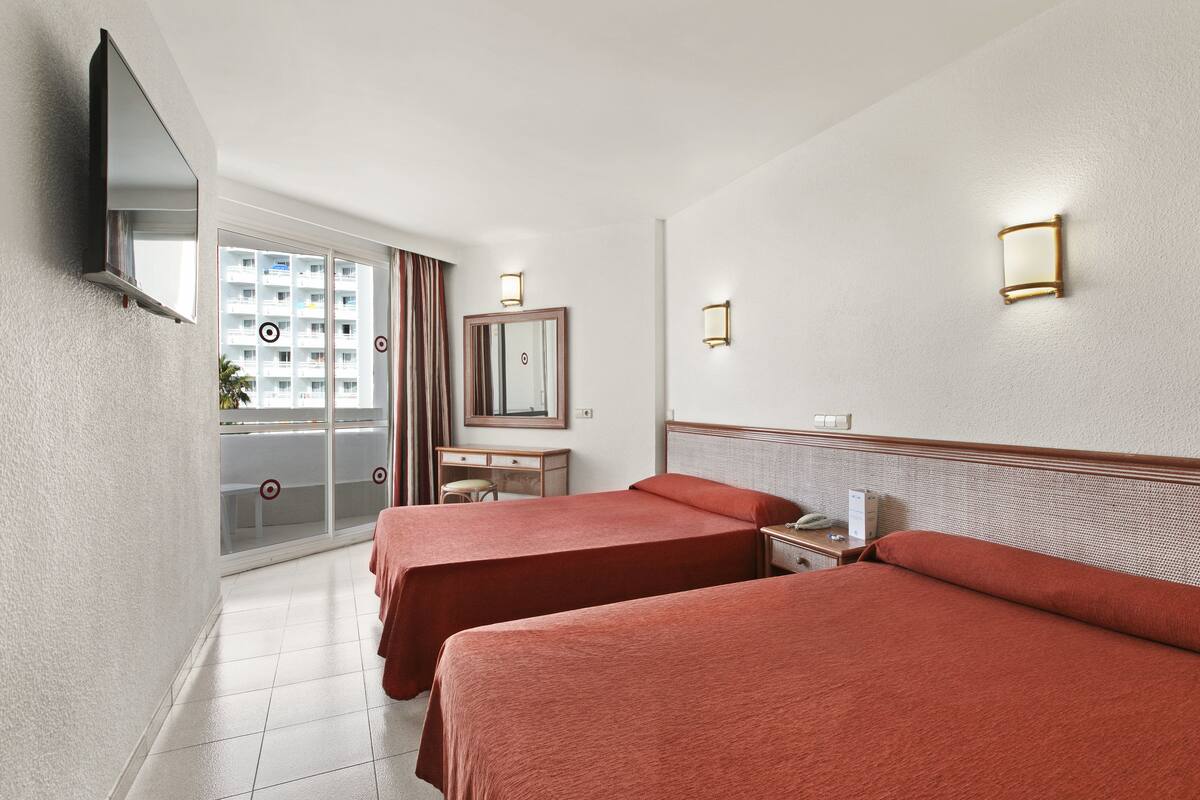 Habitación de hotel con dos camas, un escritorio, un espejo y un televisor instalado en la pared.