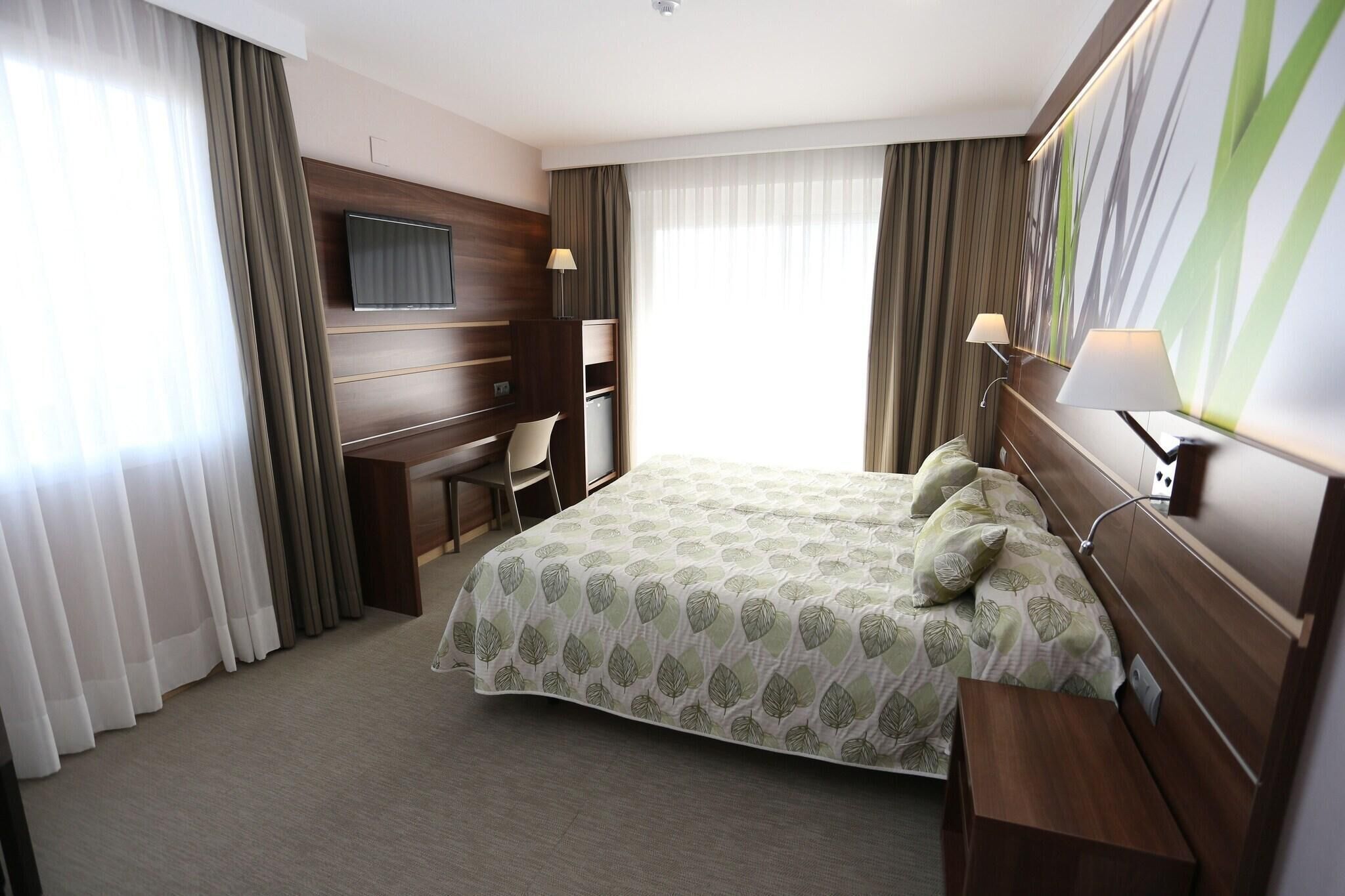 Une chambre d’hôtel avec un lit, un bureau, une chaise et un téléviseur fixé au mur.