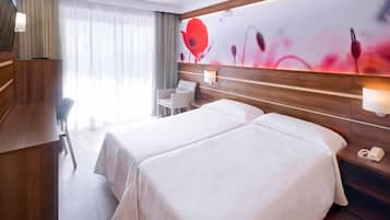 Hotellihuone, jossa on kaksi sänkyä, työpöytä, tuoli, puhelin ja seinä, joka on koristeltu kukkakuvioisella seinämaalauksella.