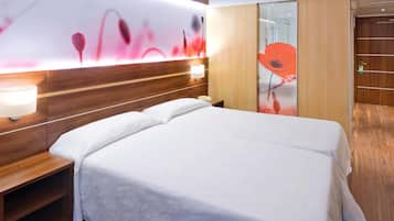 Habitación de hotel con cabecera de madera, mesita de noche con lámpara, teléfono y una cama grande con ropa blanca.