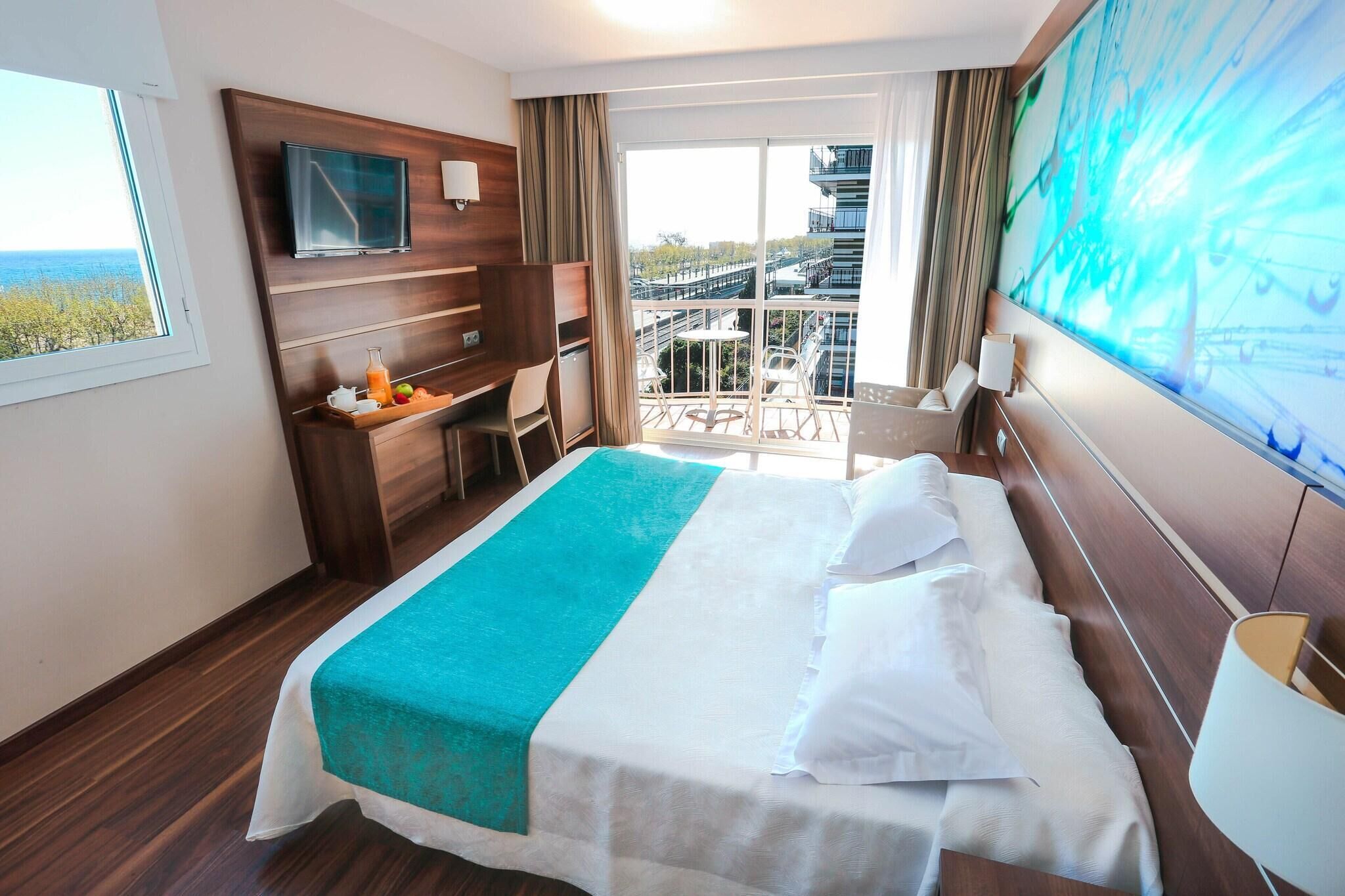 Une chambre d’hôtel comprenant un lit, une télévision, un bureau avec une chaise, un balcon avec vue et une grande fenêtre.