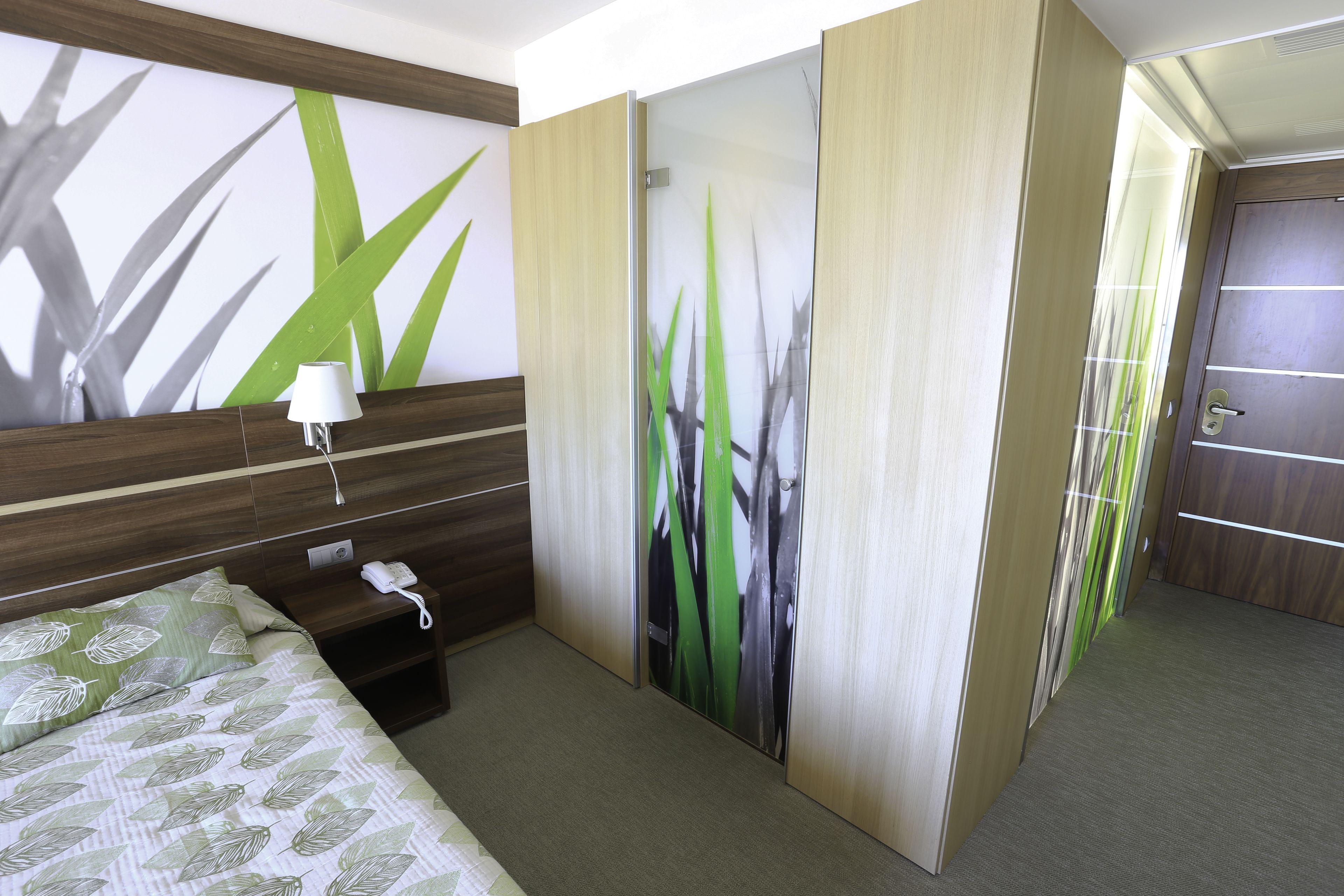 Une chambre d’hôtel avec un lit, une table de chevet avec un téléphone et un mur orné d’un motif de feuilles.