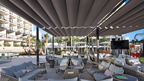 Un espace extérieur aménagé avec des meubles en osier, un téléviseur à écran plat et des parasols pour créer de l’ombre.