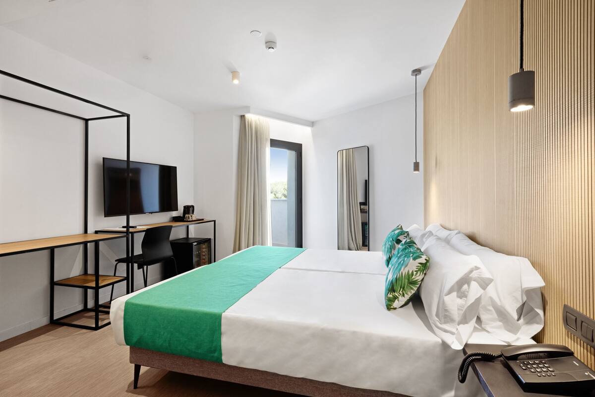 A modern hotel room with a bed, desk, chair, TV, and a view of the outdoors.