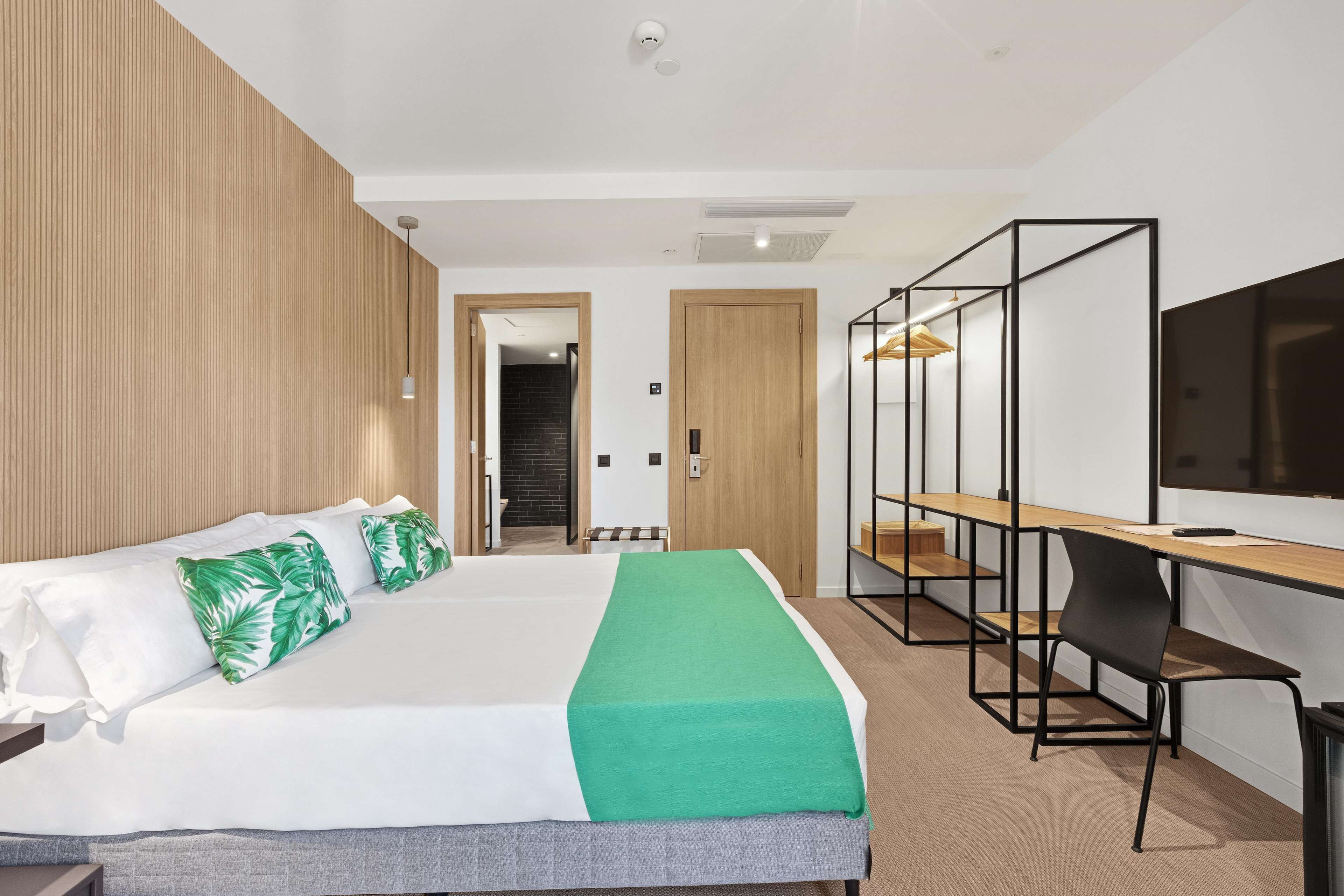 A modern hotel room with a large bed, a desk, and a TV.