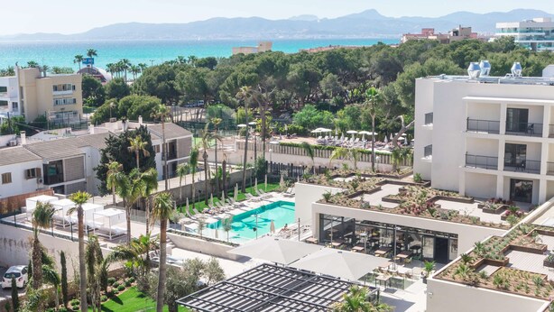 Une piscine sur le toit, offrant une vue sur la mer, et entourée de bâtiments et de verdure.