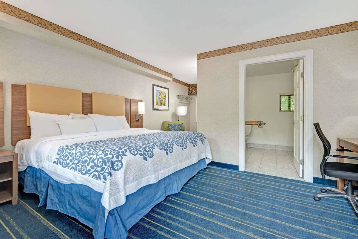 A hotel room with a large bed, a desk, and a chair. There is a door leading to a bathroom.