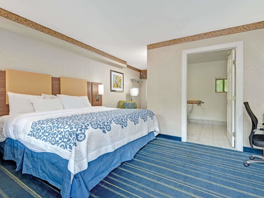 Ein Hotelzimmer mit einem großen Bett, einem Schreibtisch und einem Sessel. Eine Tür führt zu einem Badezimmer.