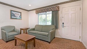 A room with a patterned carpet, a green patterned sofa, a wooden table, and a framed picture on the wall.