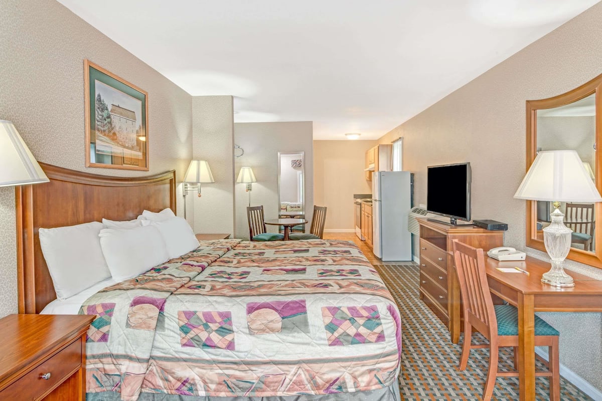 A hotel room with a large bed, a desk with a computer, a TV, and a dining area.