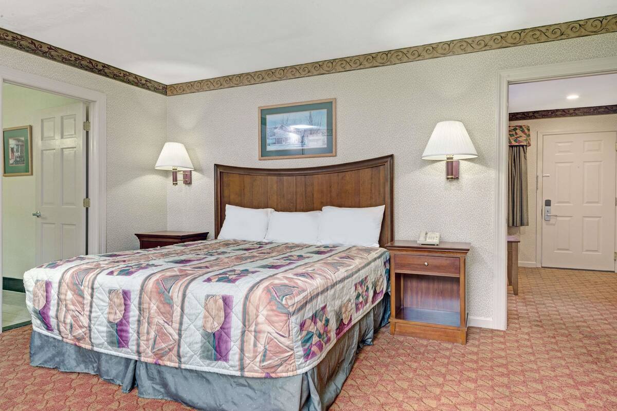 A neatly arranged bedroom with a large bed, two bedside tables with lamps, a framed picture on the wall, and a door to the left.