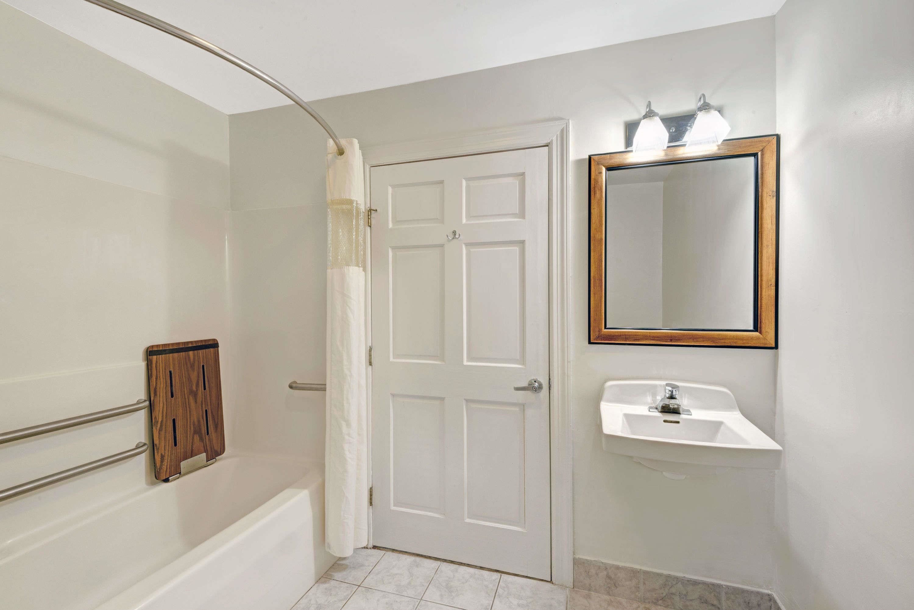 A bathroom with a white door, a wooden medicine cabinet, a white sink, and a mirror with a wooden frame.