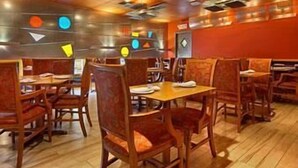 A restaurant interior with wooden tables and chairs, a red wall, and geometric ceiling decorations.