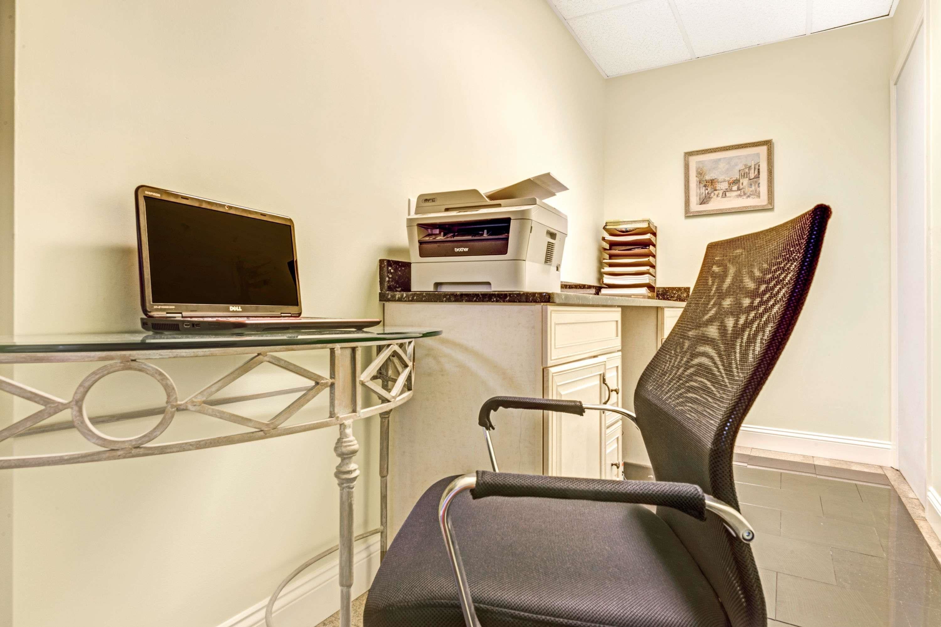 A room with a desk, a laptop, a printer, a chair, and a framed picture on the wall.