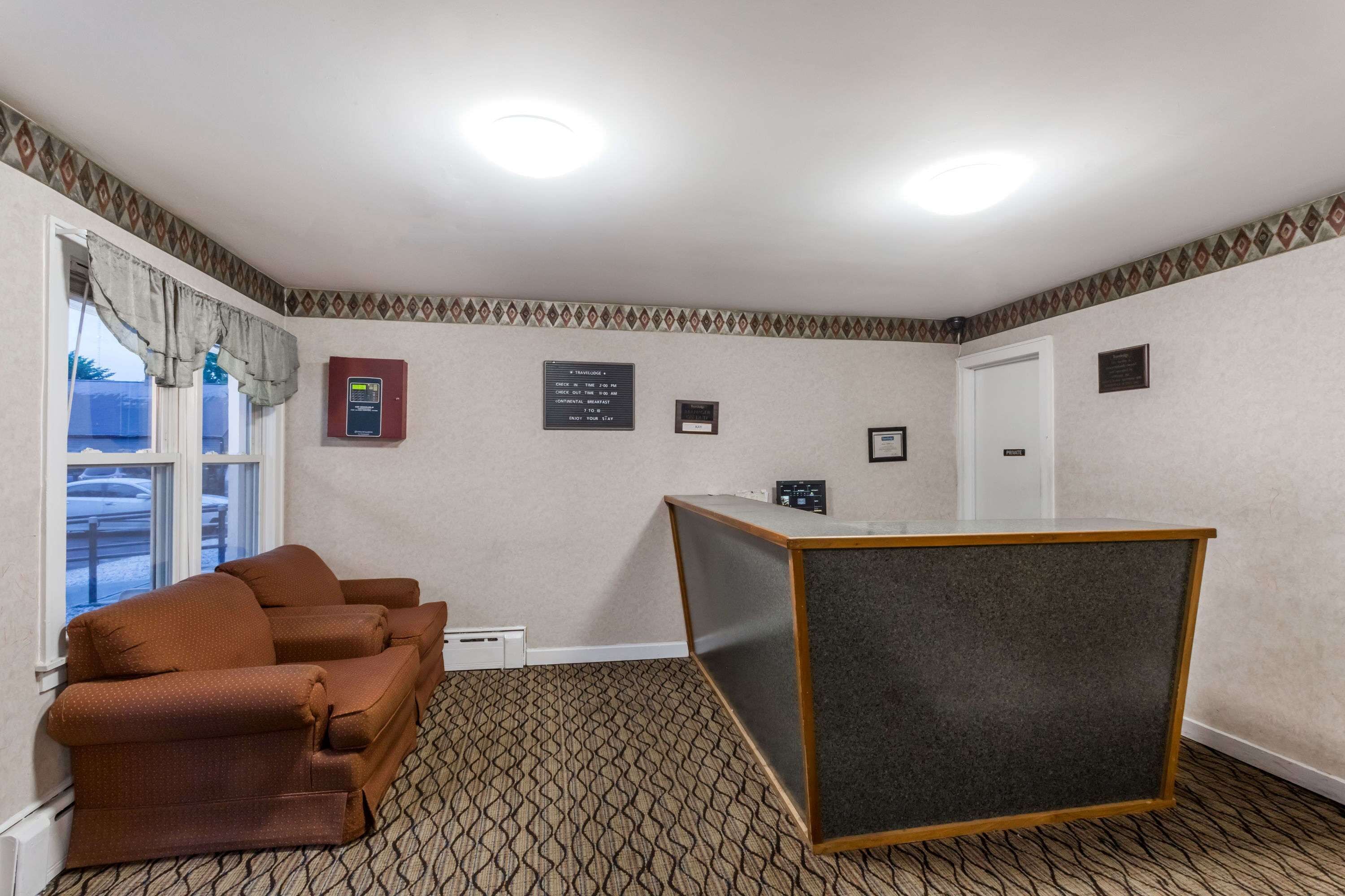 Une chambre d’hôtel avec une moquette à motifs, un canapé marron, un comptoir d’accueil et une fenêtre avec des rideaux.