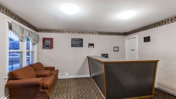 Une chambre d’hôtel avec une moquette à motifs, un canapé marron, un comptoir d’accueil et une fenêtre avec des rideaux.
