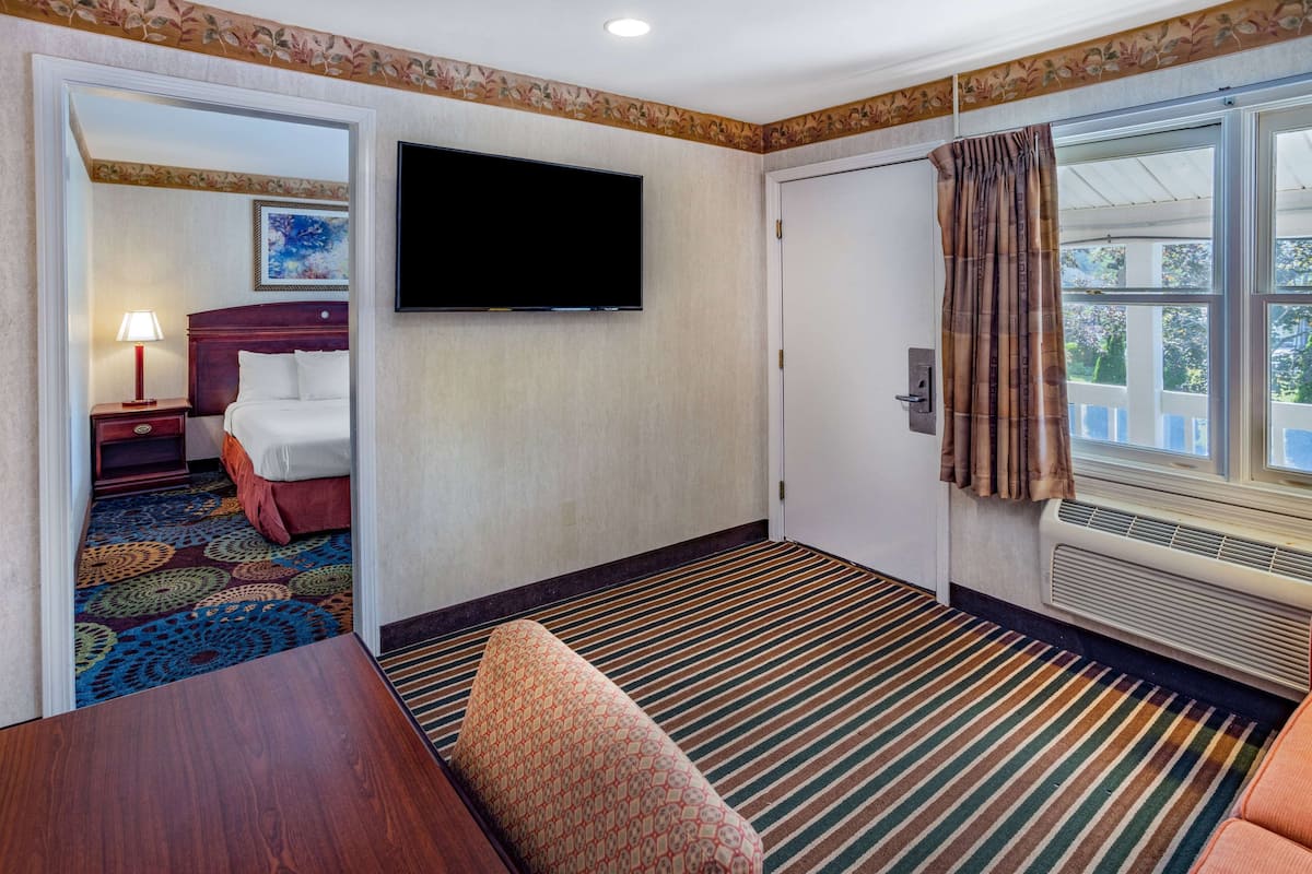 Ein Hotelzimmer mit Bett, Fernseher, einem Fenster mit Vorhängen, Teppich und einem Holztisch.