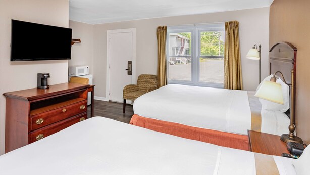 A hotel room with a large bed, a desk with a coffee maker, a chair, a TV, and a window with curtains. - Travelodge by Wyndham Great Barrington Berkshires (Great Barrington)