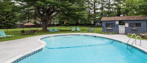 A swimming pool with a tiled edge, surrounded by lounge chairs and a small building with a sign.