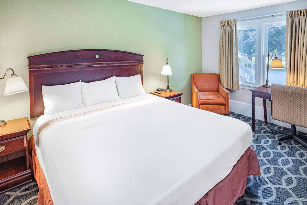 Ein Hotelzimmer mit einem großen Bett, einem Schreibtisch, einem Sessel und Blick ins Freie.