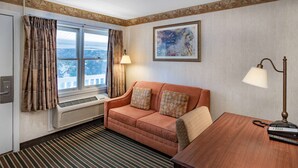 A hotel room with a sofa, a wooden table, a lamp, a telephone, and a painting on the wall. - Travelodge by Wyndham Great Barrington Berkshires (Great Barrington)