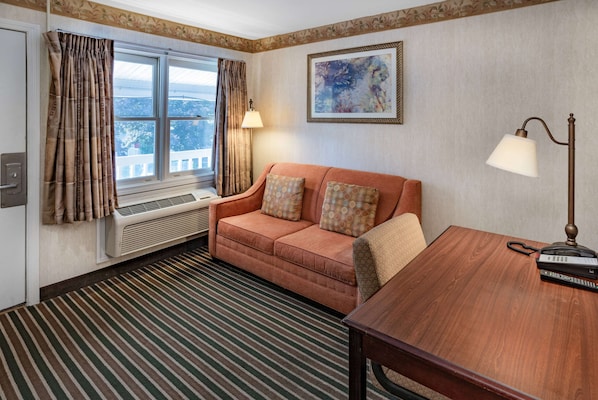 Ein Hotelzimmer mit einer Sitzecke, einem Holztisch, einer Lampe, einem Telefon und einem Bild an der Wand.