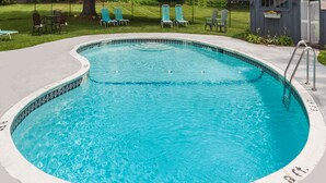 A circular pool with a tiled edge, surrounded by a concrete deck and a grassy area with chairs and a small shed. - Travelodge by Wyndham Great Barrington Berkshires (Great Barrington)