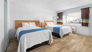 Et hotelværelse med to senge, en træsenggavl, et vindue med gardiner og udsigt til gaden.