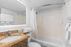 A bathroom with a granite sink, white tiles, a bathtub, and a shower curtain. - Atlantic Inn (Virginia Beach)