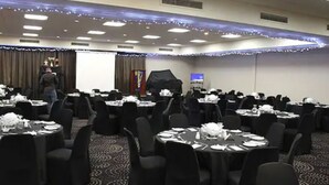 A conference room with round tables, black chairs, and a stage with a podium. - Kalgoorlie Overland Motel (Somerville)