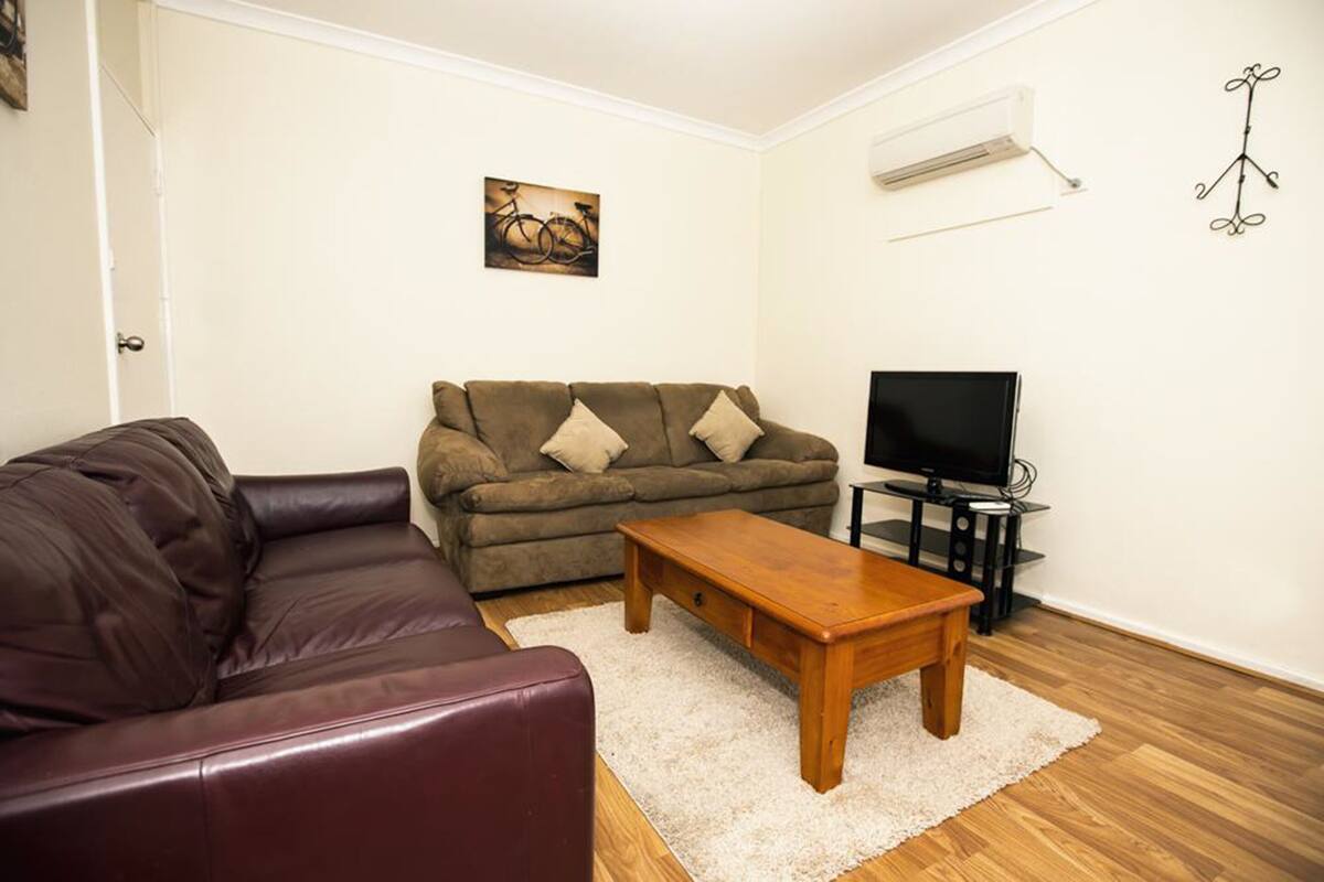 Una sala de estar con un sofá de cuero marrón, una mesa de centro de madera, un sofá beige y un televisor sobre un mueble.