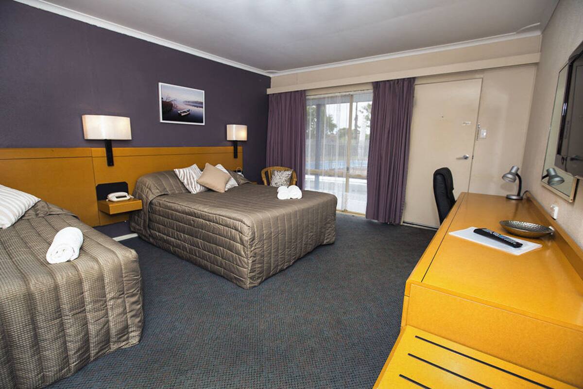 Habitación de hotel con dos camas, un escritorio, una silla, un televisor y una ventana con cortinas.