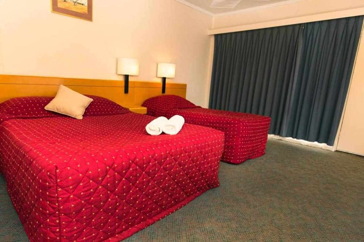 Una habitación de hotel con una cama grande, dos lámparas de noche, una mesita y una ventana con cortinas.
