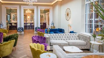 A spacious lobby with a bar area, multiple seating options including a large sofa and colorful chairs, and a chandelier.