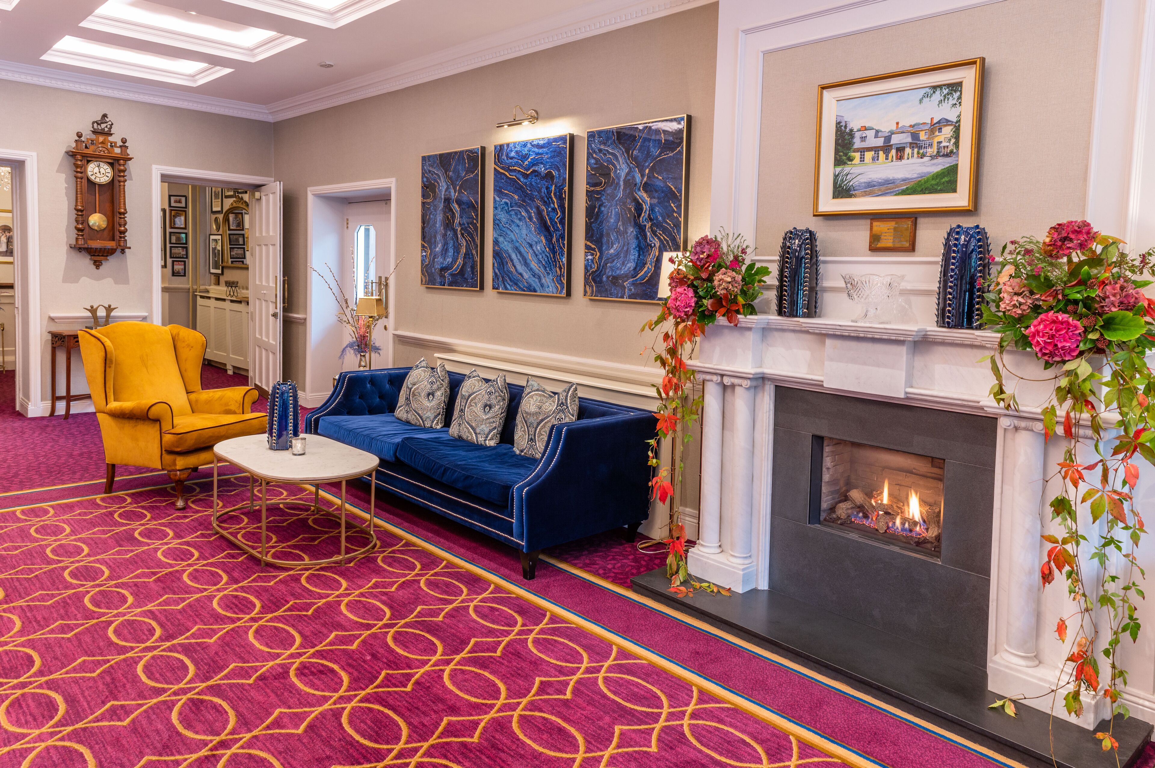 A room with a blue sofa, yellow armchair, fireplace, and a patterned carpet.