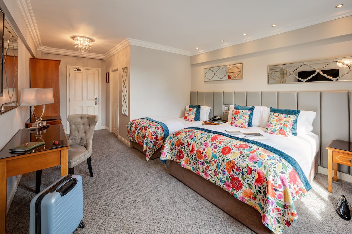 A hotel room with two beds, a desk, a chair, and a suitcase.