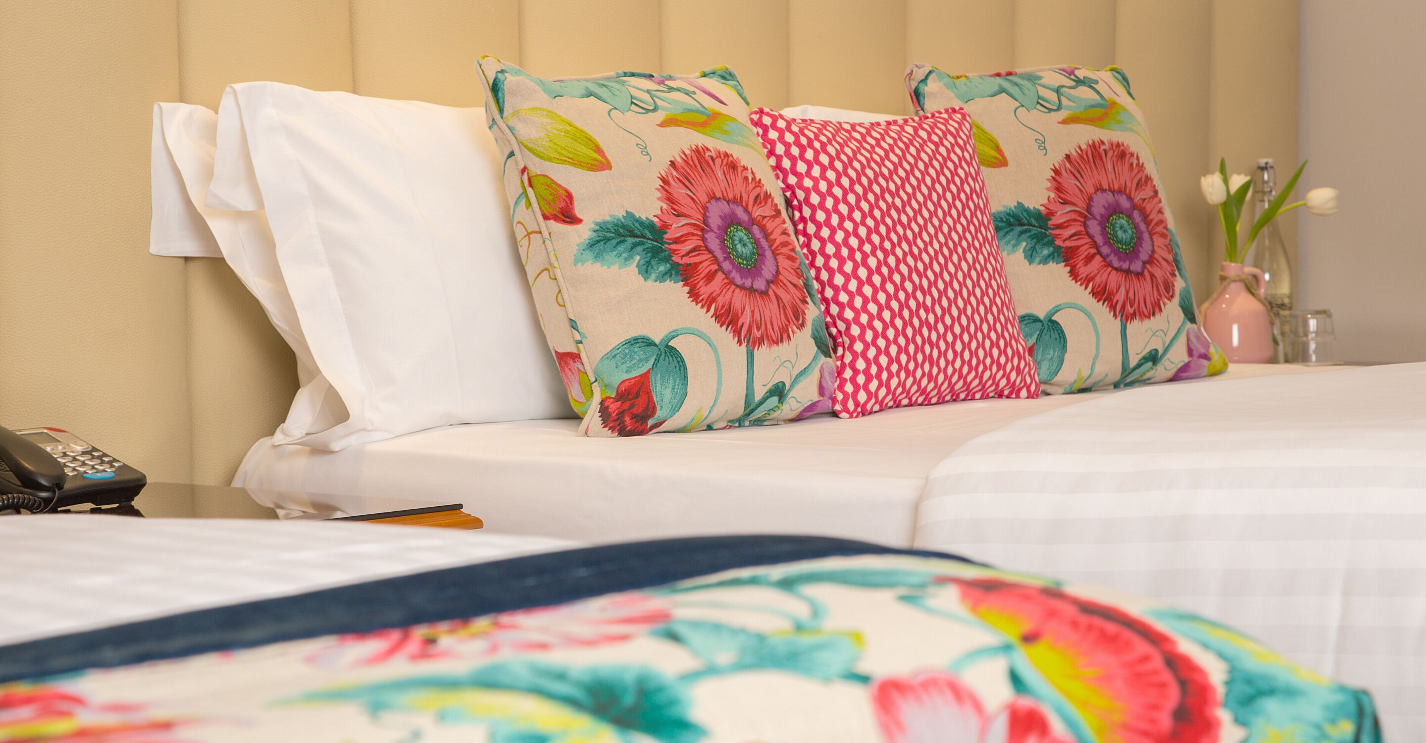 A hotel room with a bed, a telephone, and a vase with flowers.