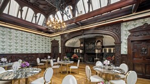 Uma sala de jantar com mesas redondas, cadeiras brancas e um candelabro.