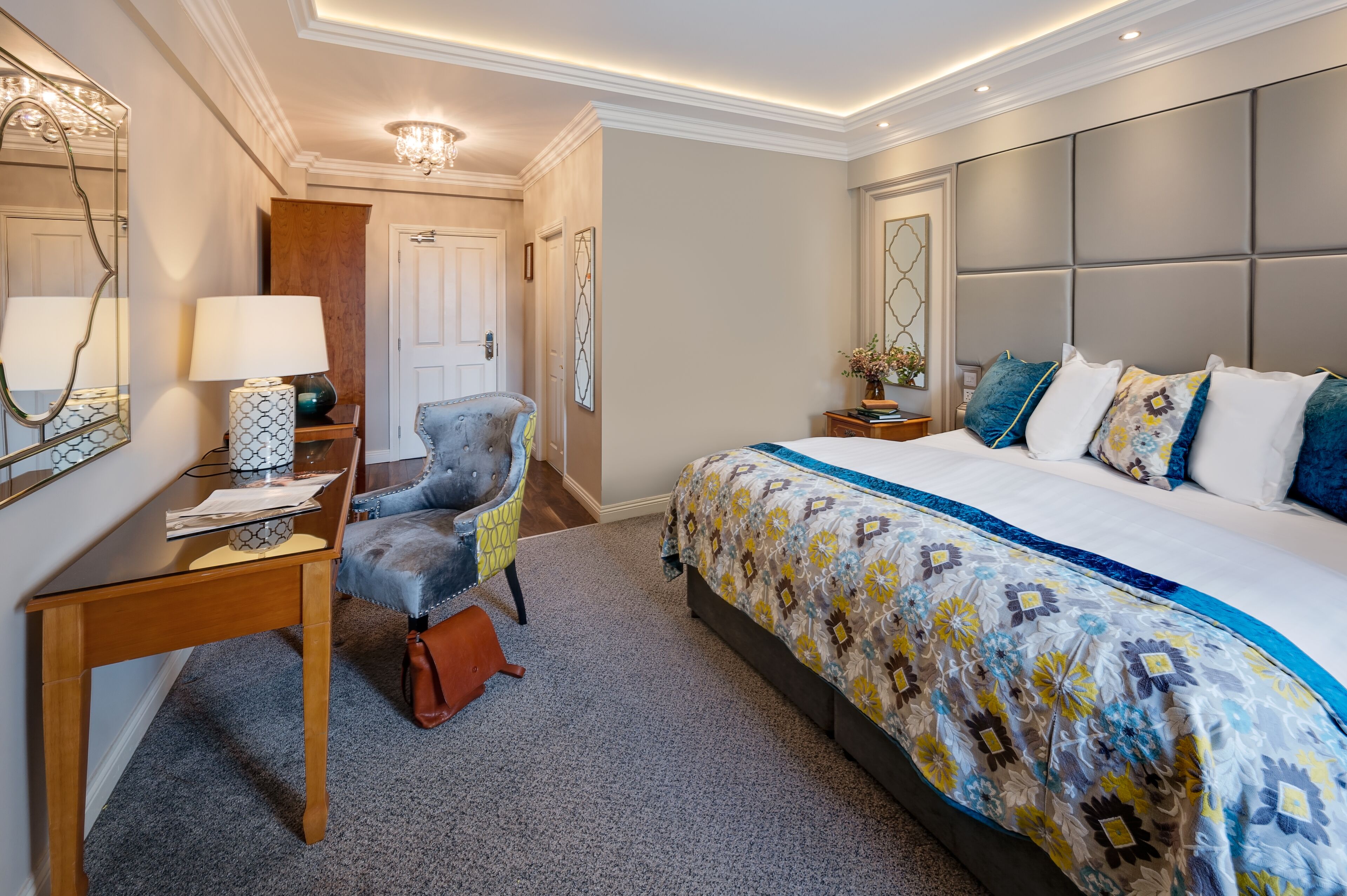 Una habitació d'hotel amb un llit gran, una taula amb una làmpada, una cadira i un mirall.