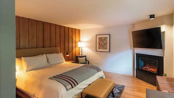 A modern hotel room with a large bed, a flat-screen TV, a fireplace, and a wooden headboard.