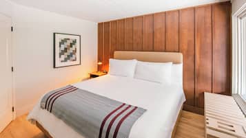 A neatly arranged bedroom with a large bed, a wooden headboard, a bedside table with a lamp, and a framed artwork on the wall.